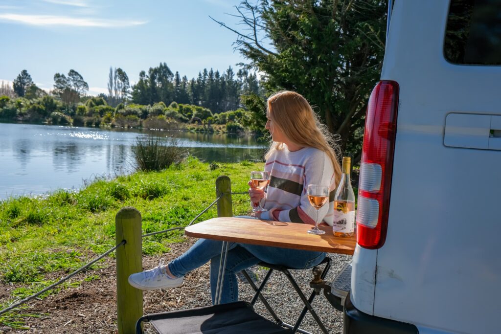 Lakeside view enjoying a glass of wine at the back of a converted campervan. 