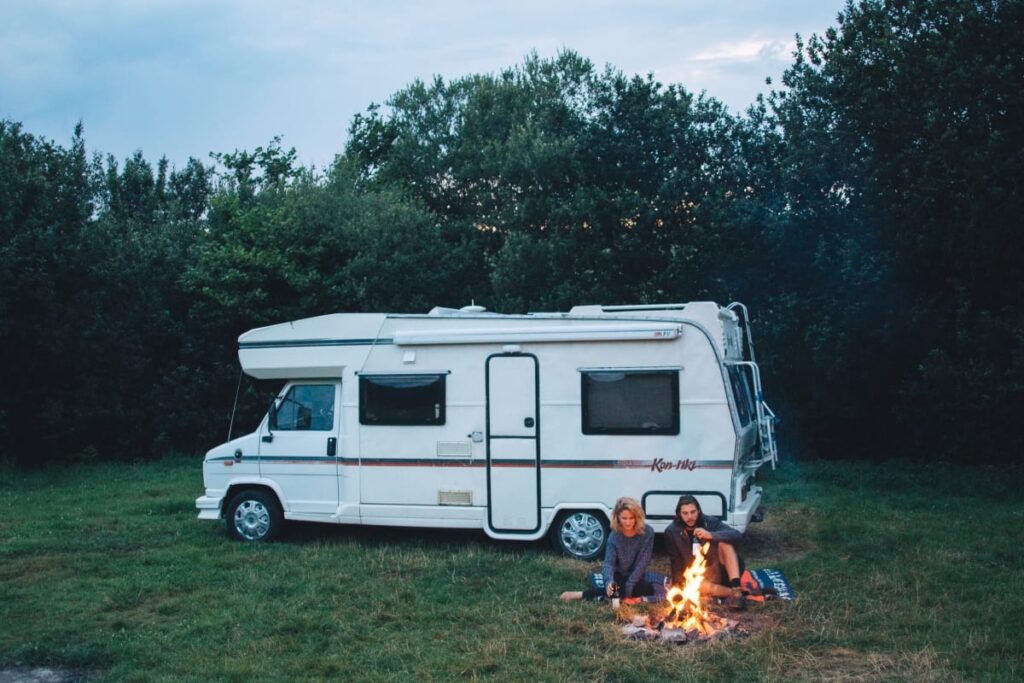 A couple having a campfire in front of a retro campervan