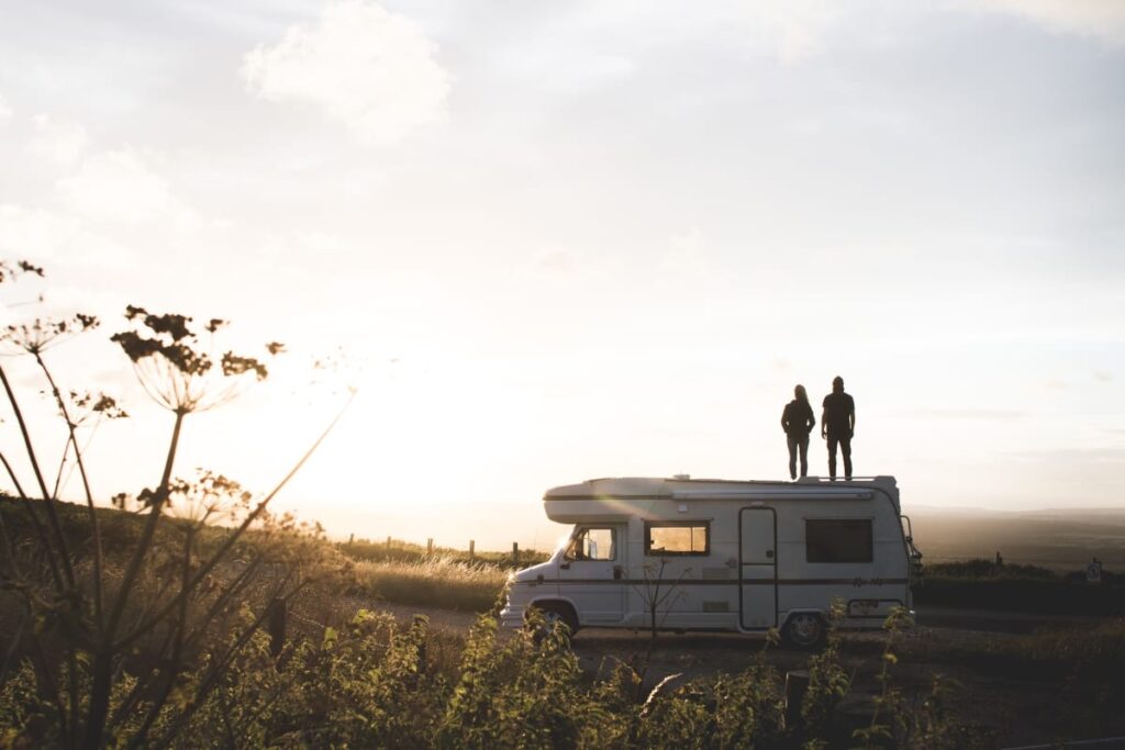 The silhouette of a couple standing on top of Tiki the retro campervan in a field