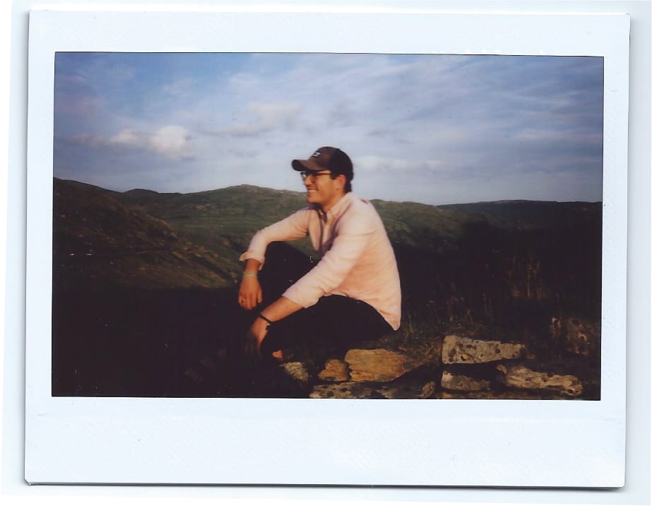 a Polaroid of a man sat on a rock in wales