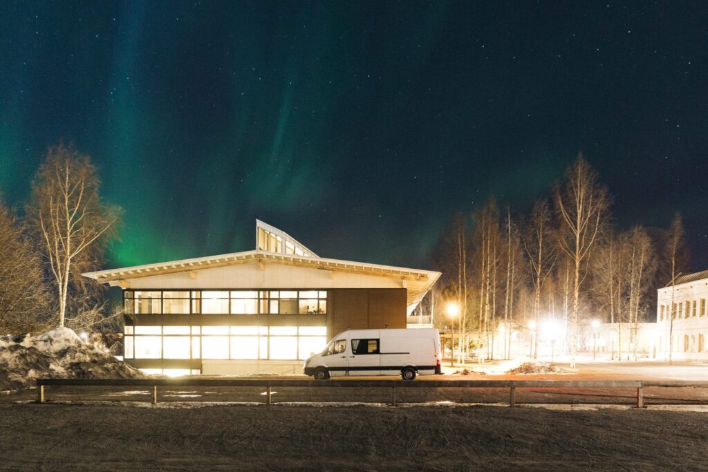 a campervan parked on the roadside at night with northern lights in the background