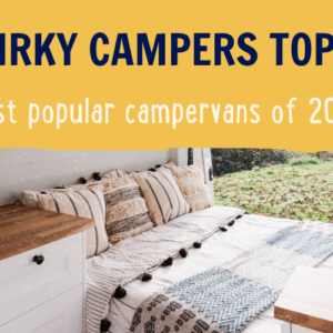 A cozy campervan interior with a made bed featuring patterned pillows and blankets. The van has wooden cabinets and a natural wooden surface near the bed. The window reveals a scenic outdoor view of grass and trees. Overlaid text reads, "QUIRKY CAMPERS TOP 10: Most popular campervans of 2023.