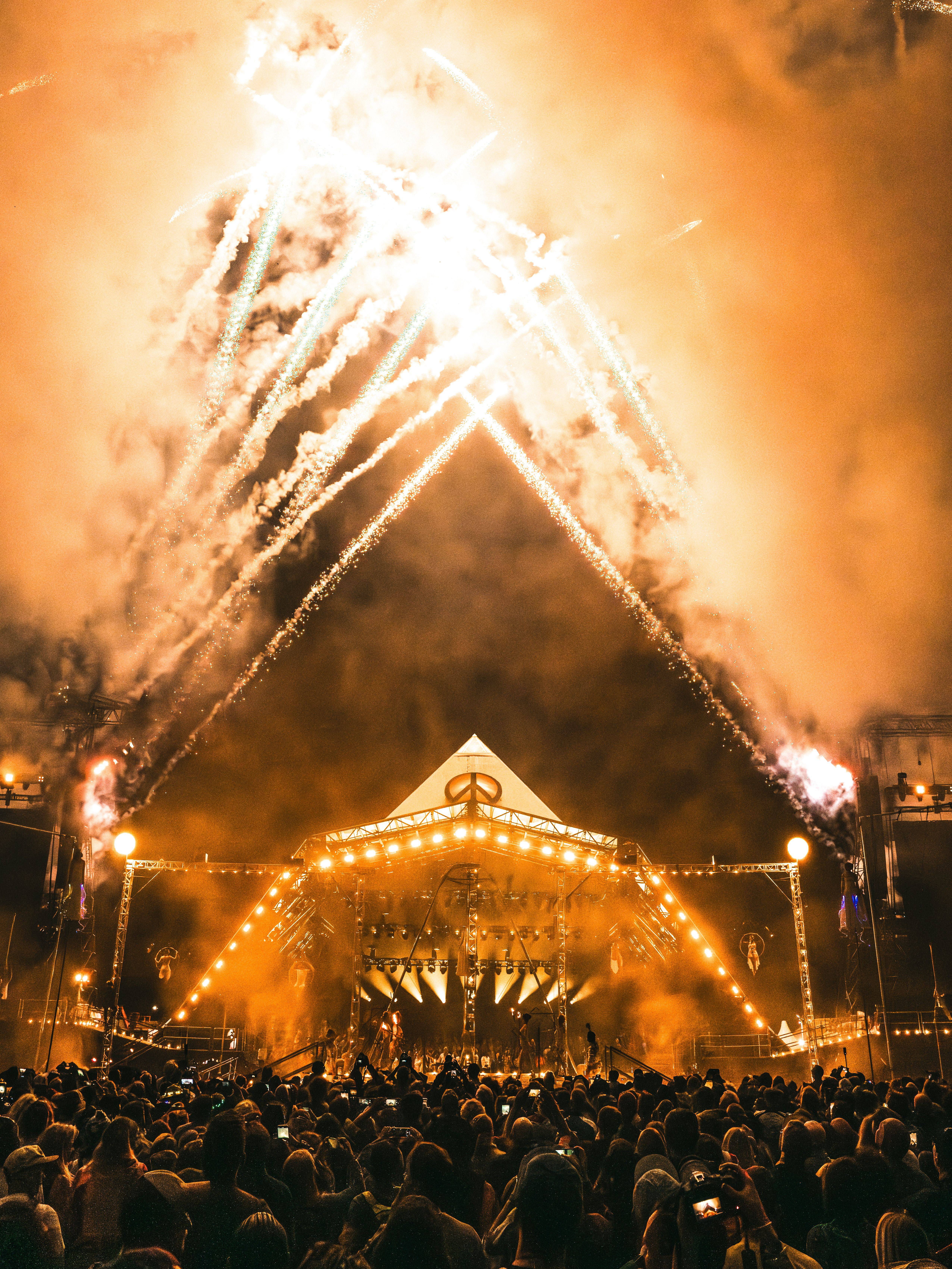 The pyramid stage at Glastonbury Festival lit up with fire works and orange lighting. A large crown stands infront the stage