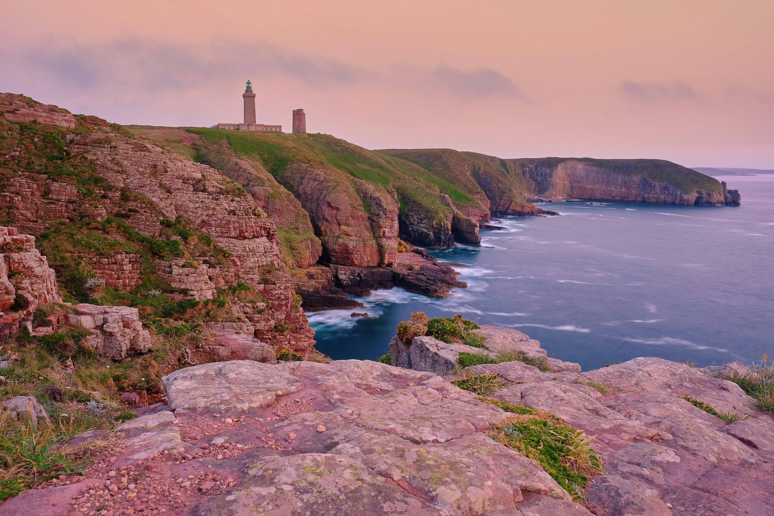 A tall lighthouse perched on a cliff, with the ocean stretching out beneath it and a bright sky above.