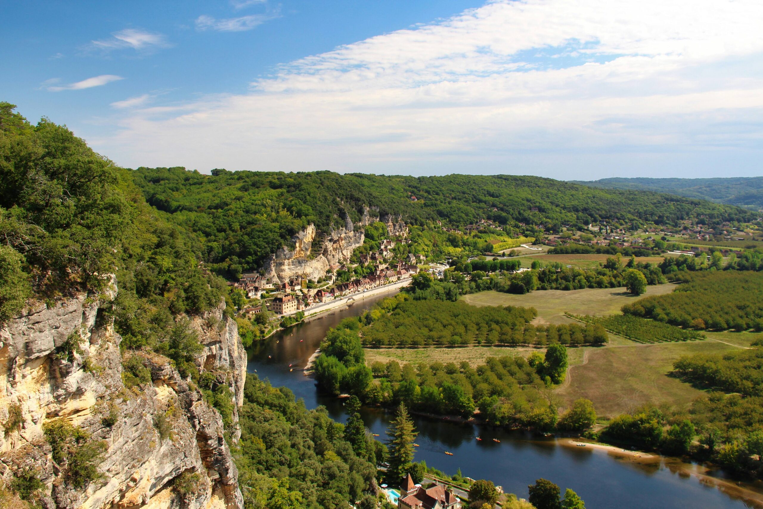 A scenic view of a river winding through lush green fields and cliffs under a blue sky with clouds.