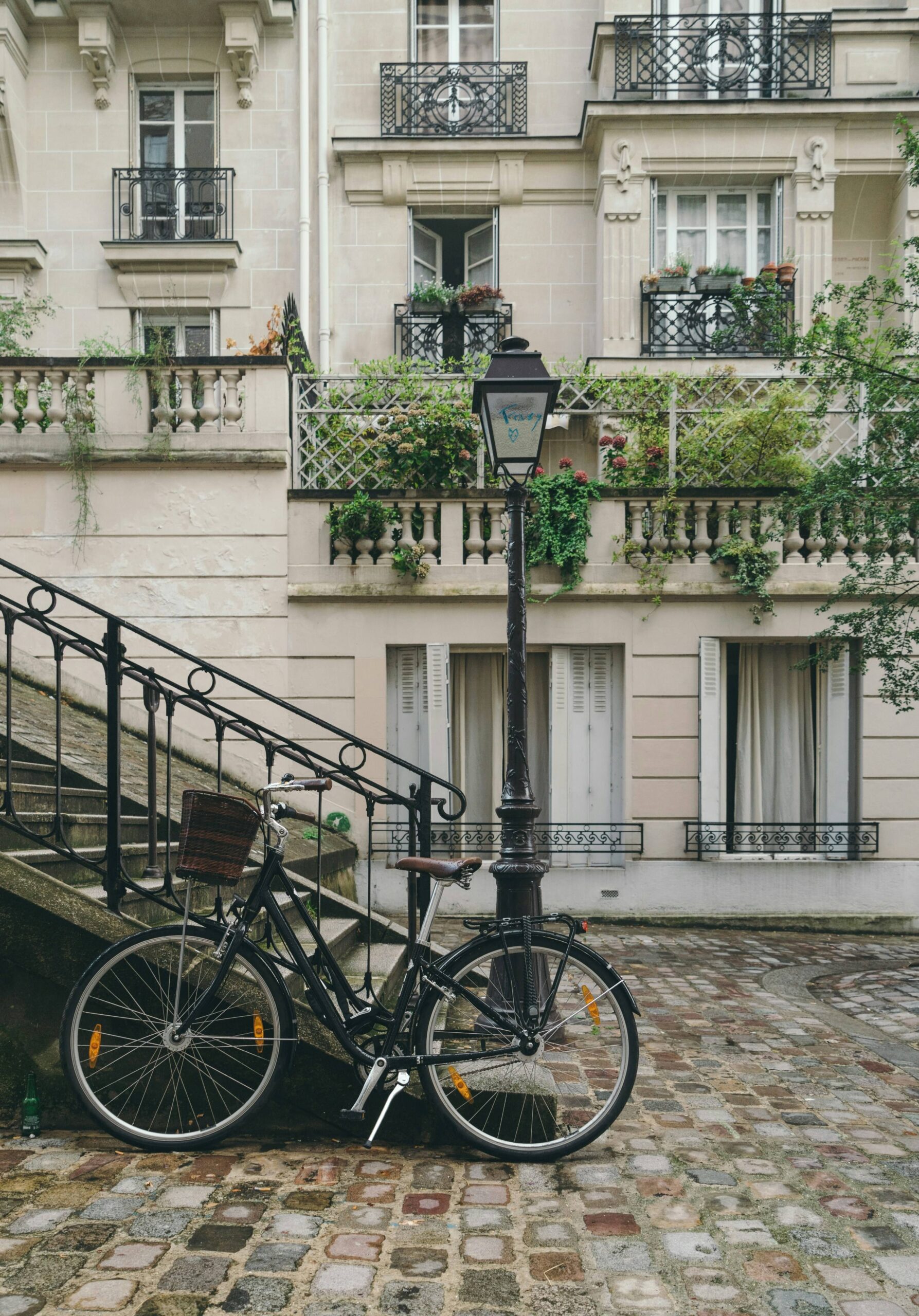 A bicycle propped against a street lamp. In the background are some light bricked apartments with greenery on the balconies