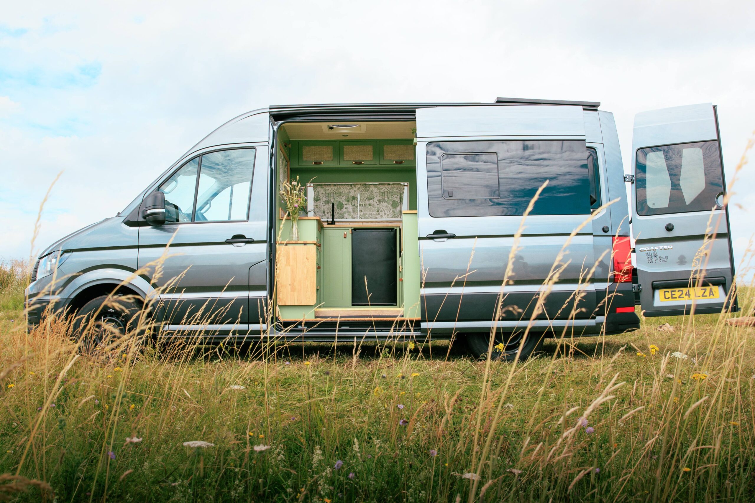 Handcrafted campervan parked on grassy field with it's doors open
