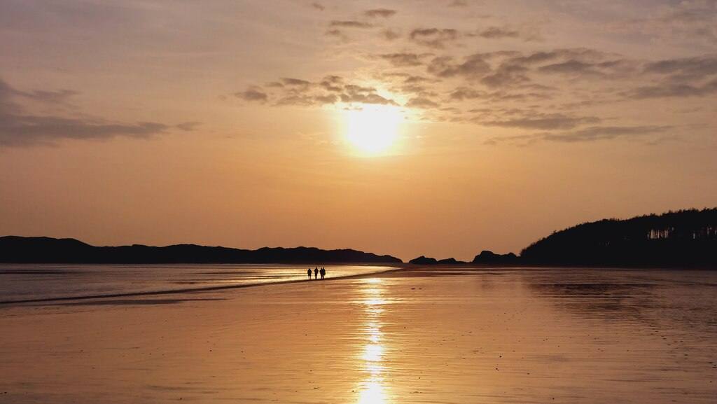 Black rock sands during sunset with people walking on the beach in the distance