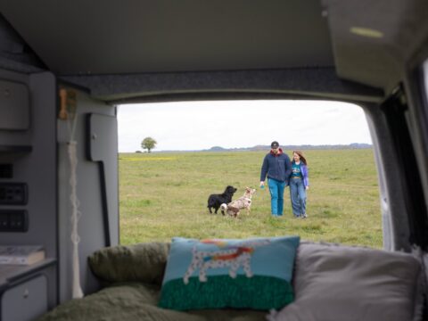 Image taken from inside a campervan looking onto a couple walking with dogs