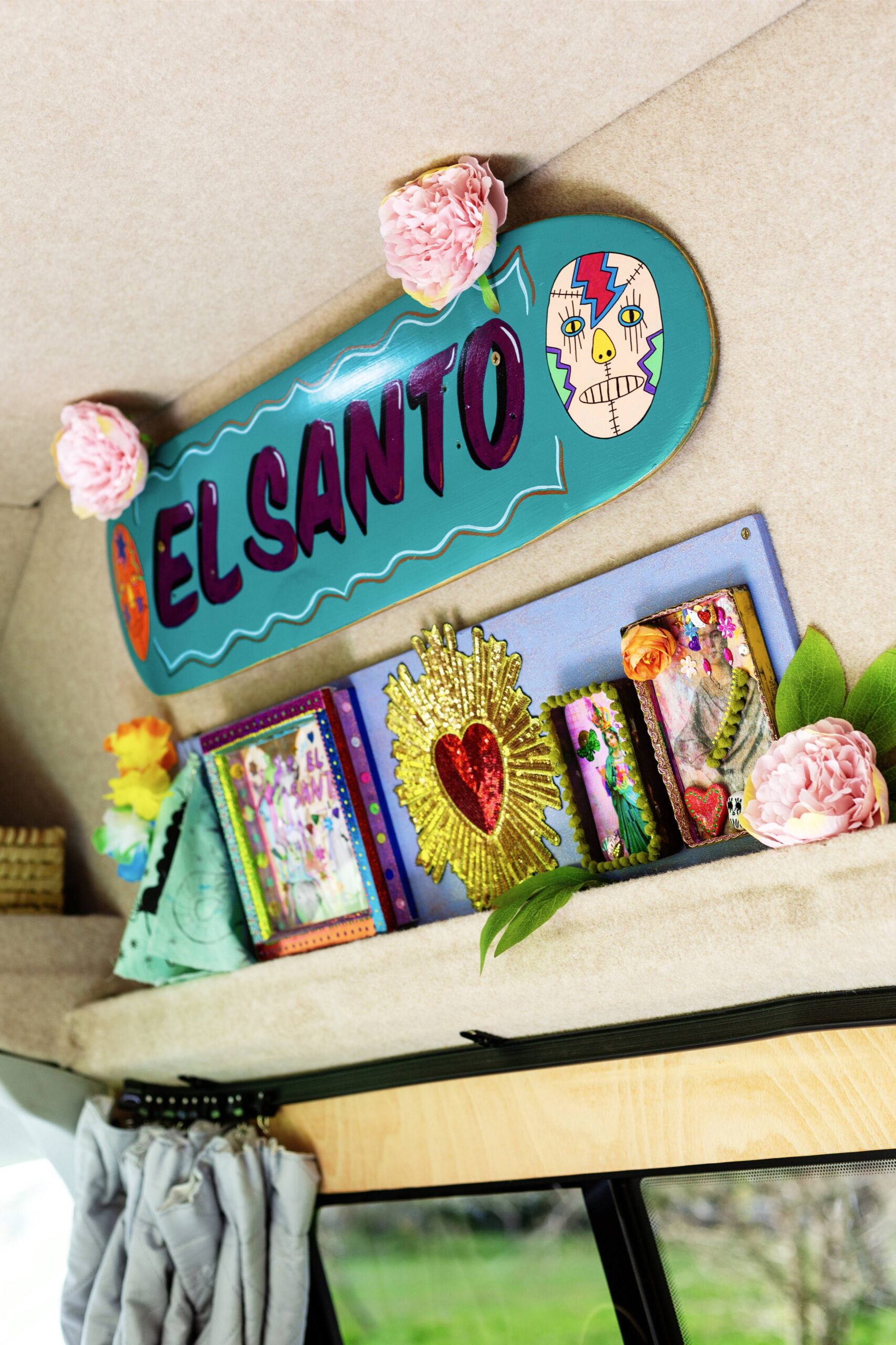 A colorful interior display featuring a sign that says "EL SANTO," along with decorative items including framed pictures and flowers on a shelf.