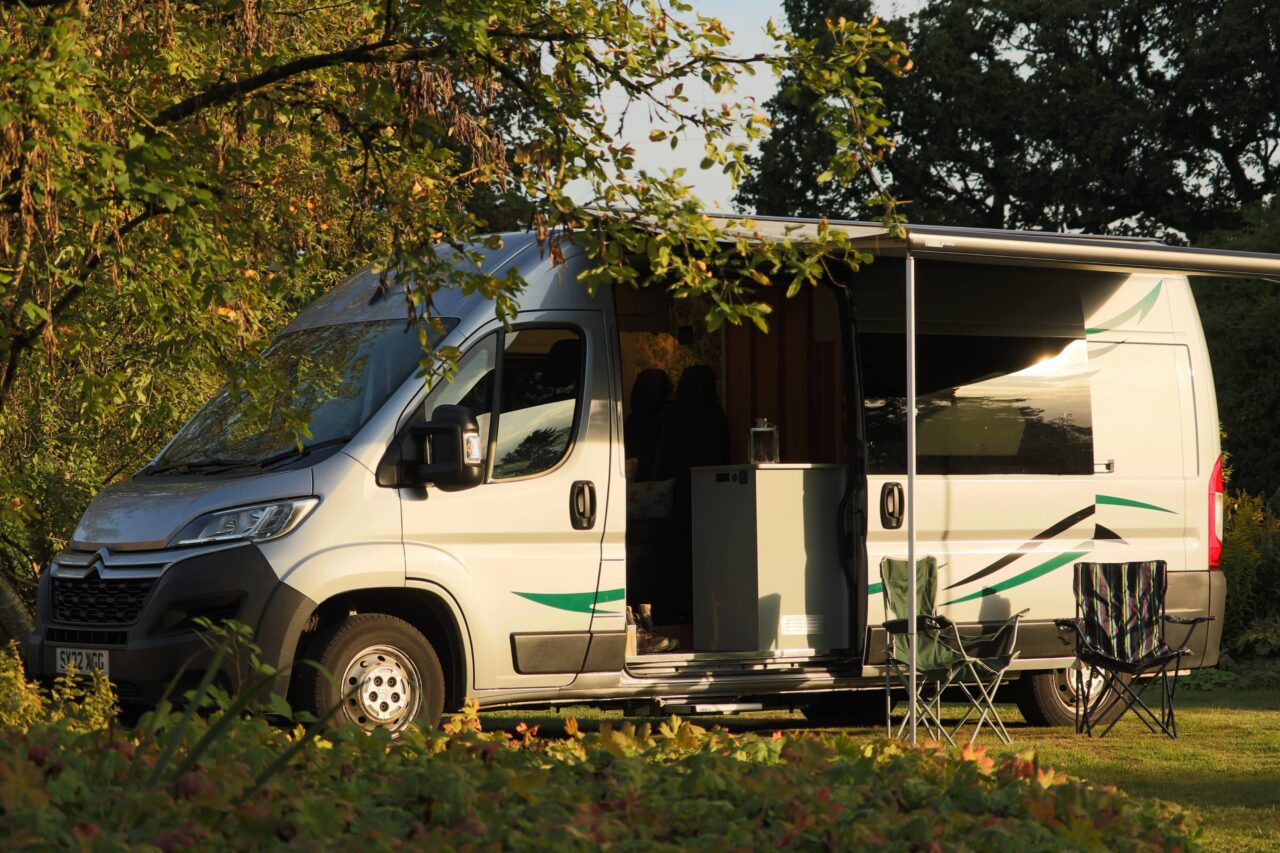A parked van in a lush green field, with a few trees visible in the distance against a bright sky.