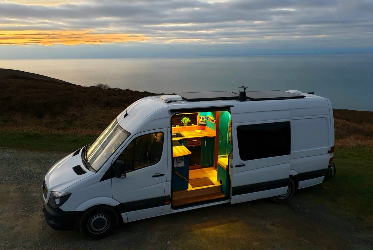 An open-door camper van at sunset, casting a warm glow in the evening light.